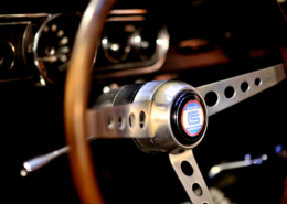 Shelby steering wheel with three spoke brushed chrome center attached to classic wooden steering wheel frame. black blur dash in the background