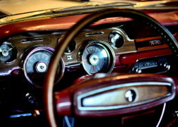 classic mustang steering wheel focus on the background a dashboard in burgundy and dark brown wood grain combination surrounding the speedometer, fuel gauge air vents and lighter