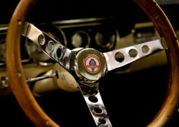Cobra classic stering wheel with three spoke brushed chrome center attached to classic wooden steering wheel frame. cream blur dash in the background with black inset dials around the instrument panel